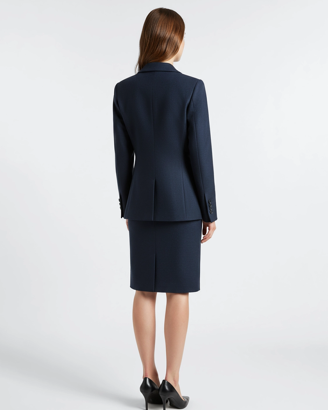 Rear view of a woman in a navy business suit and heels, standing against a neutral background.