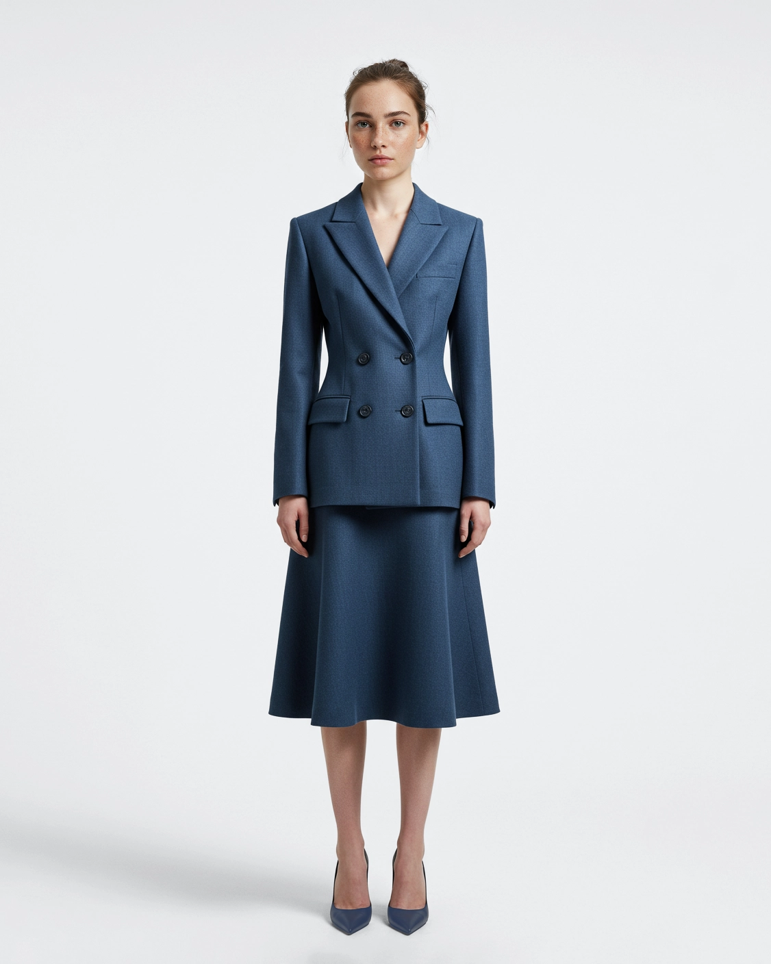 Woman in blue tailored suit and skirt standing against plain background.