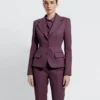 Woman in stylish purple suit standing confidently against a simple background.