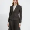 Woman in tailored dark suit with pleated skirt, white shirt underneath. Professional attire on a plain background.
