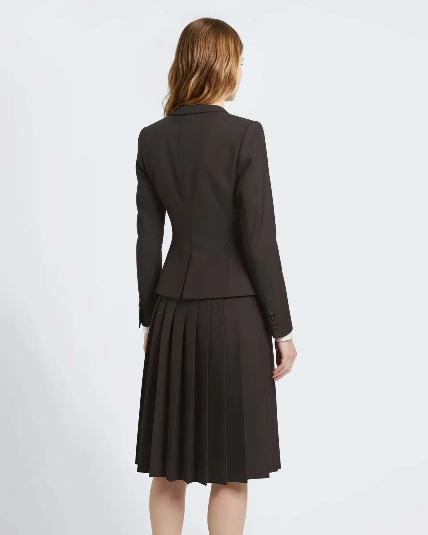 Back view of woman in black tailored jacket and pleated skirt on white background.
