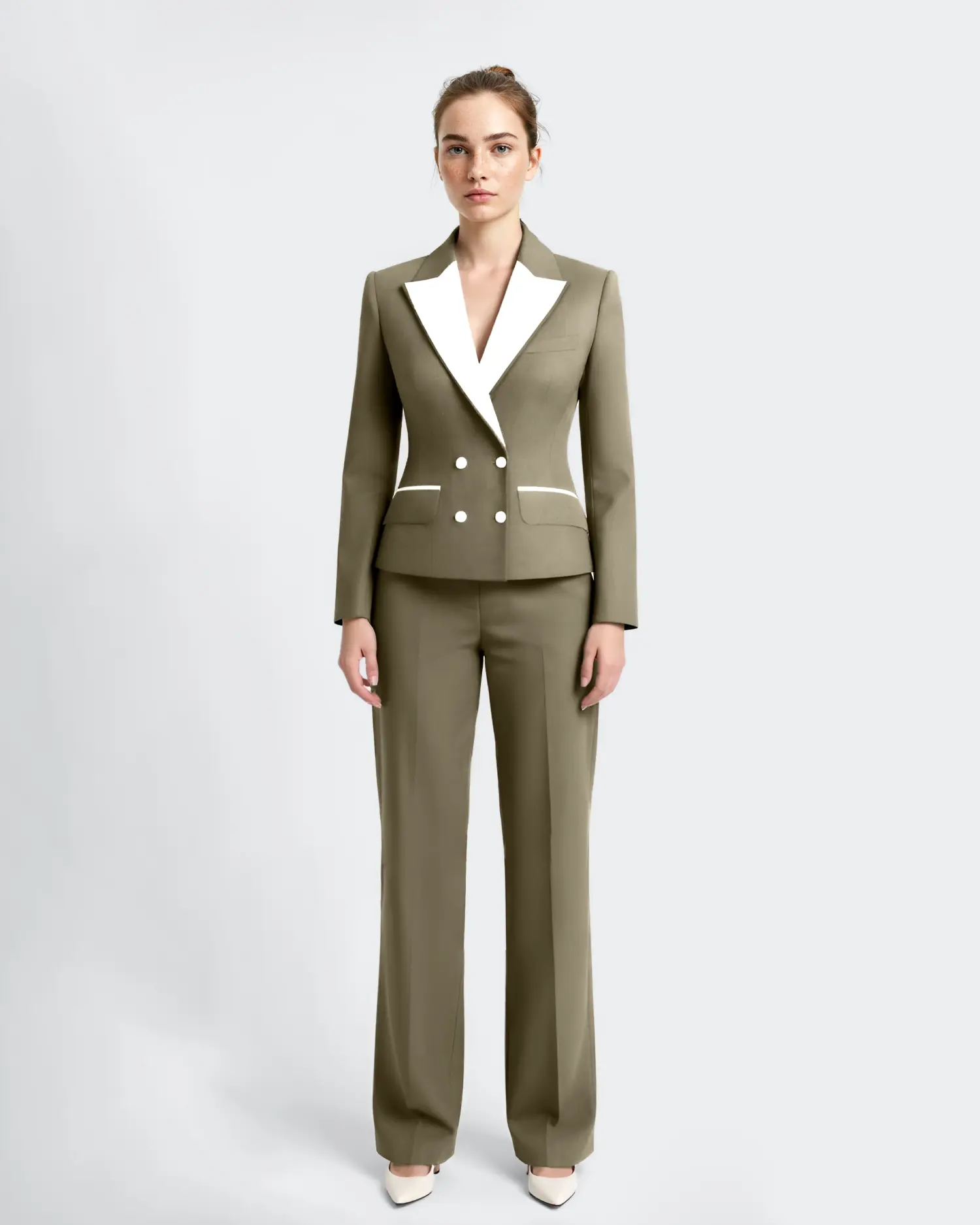 Businesswoman in olive suit with white lapels stands confidently against a neutral background.