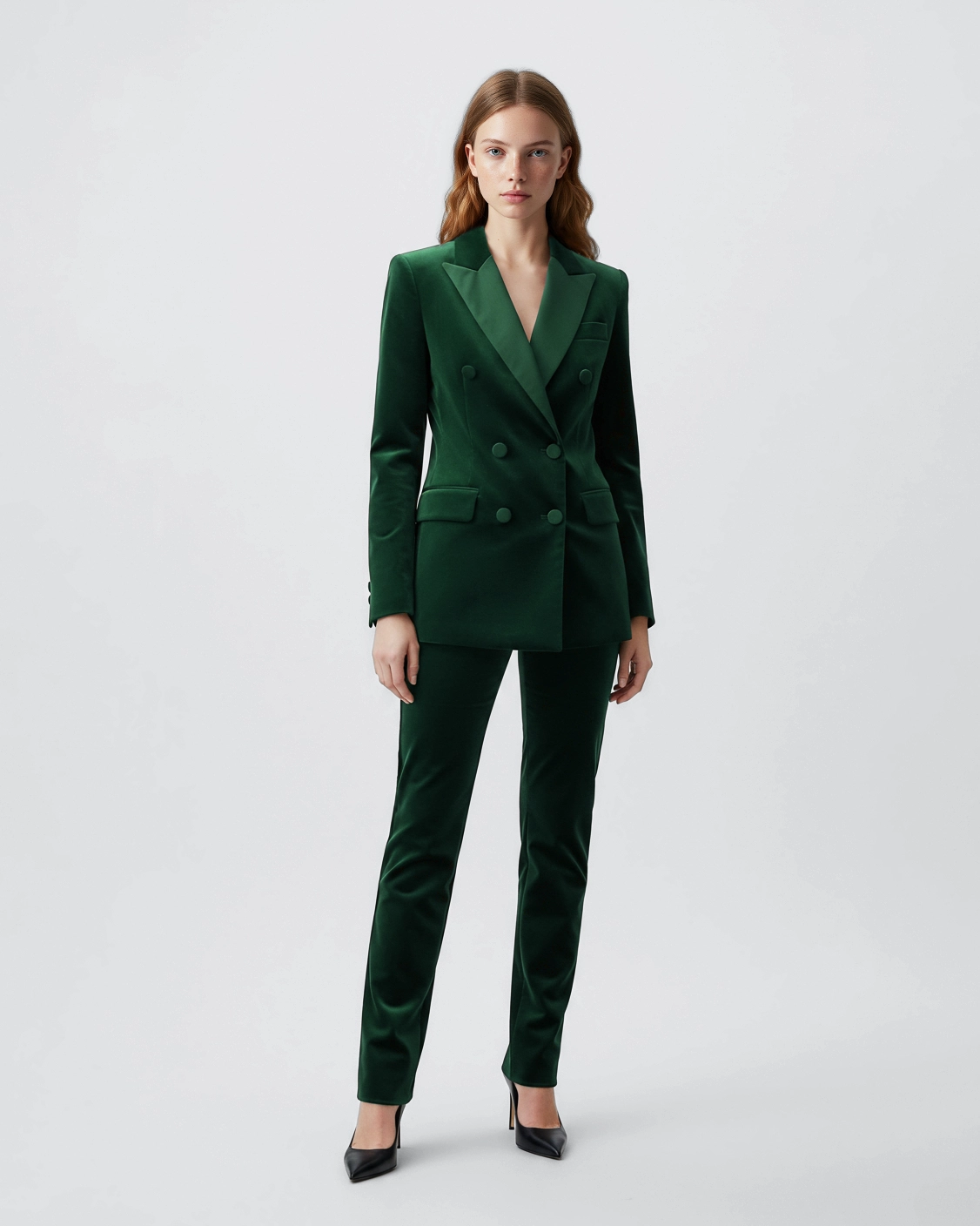 Woman wearing an elegant green suit with black heels, standing against a white background, showcasing formal fashion.