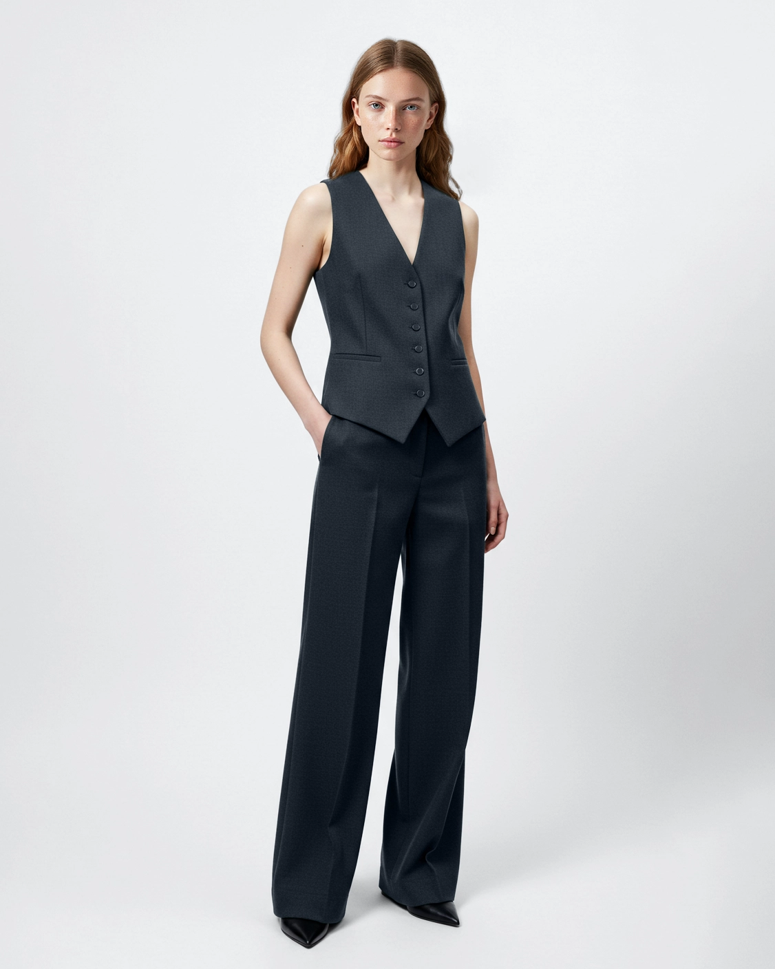 Woman in a stylish dark gray vest and wide-leg trousers, showcasing elegant fashion on a plain white background.