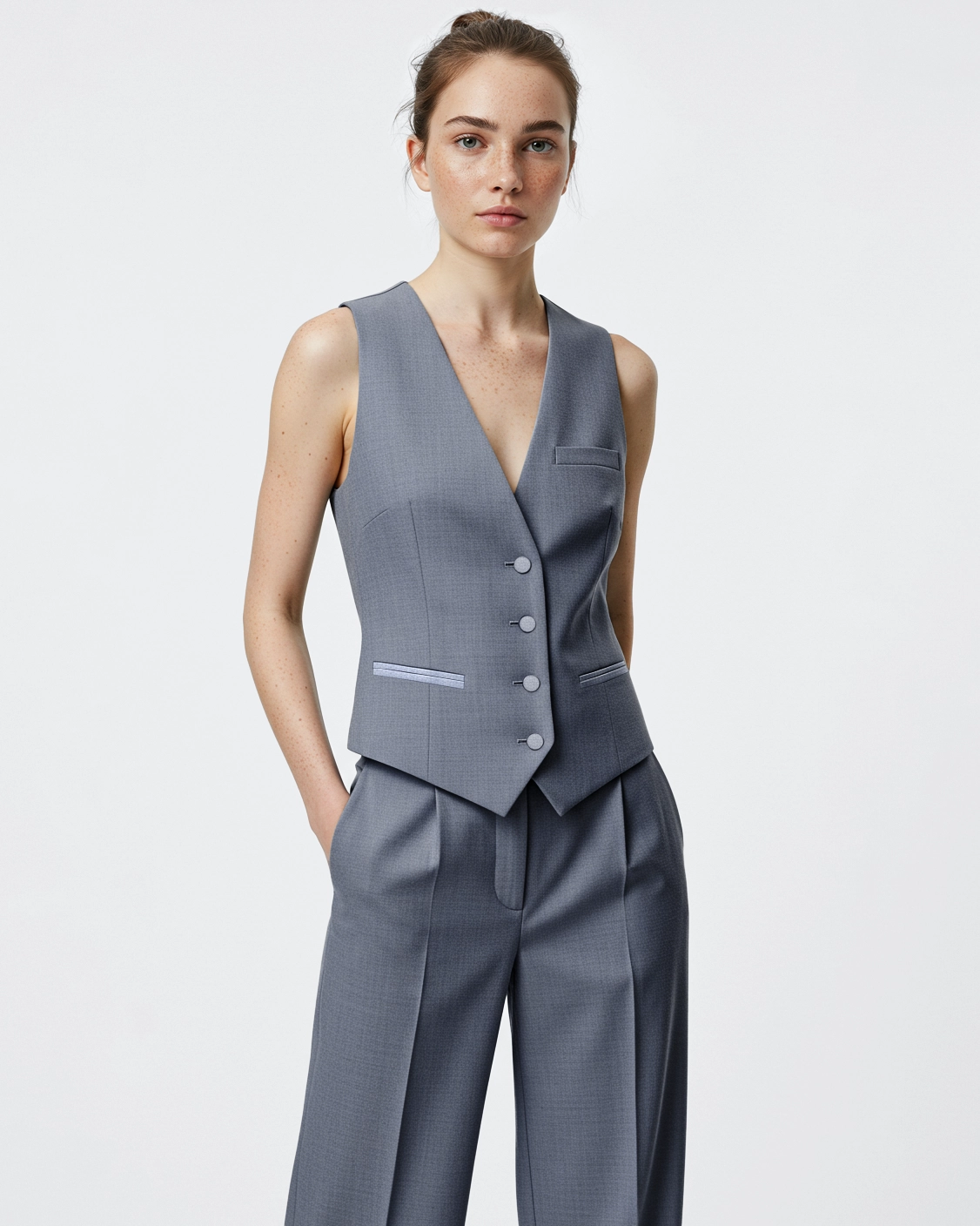 Young woman in gray tailored vest and trousers against a plain background, showcasing modern business fashion.