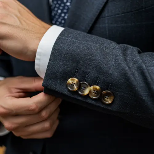 Adjusting the cuff of a bespoke tailored suits jacket with beige buttons, conveying elegance and attention to detail.