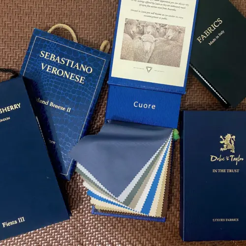 Collection of luxury fabric swatch books on textured background, showcasing diverse colors and textures for tailoring.