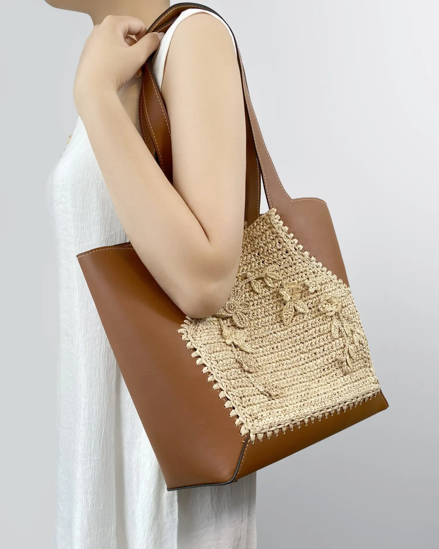 Woman holding a stylish brown and woven tote bag over shoulder, wearing a white dress. Perfect for casual outings.