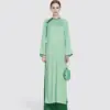 Woman in elegant green long dress with round purse, standing against a plain background.