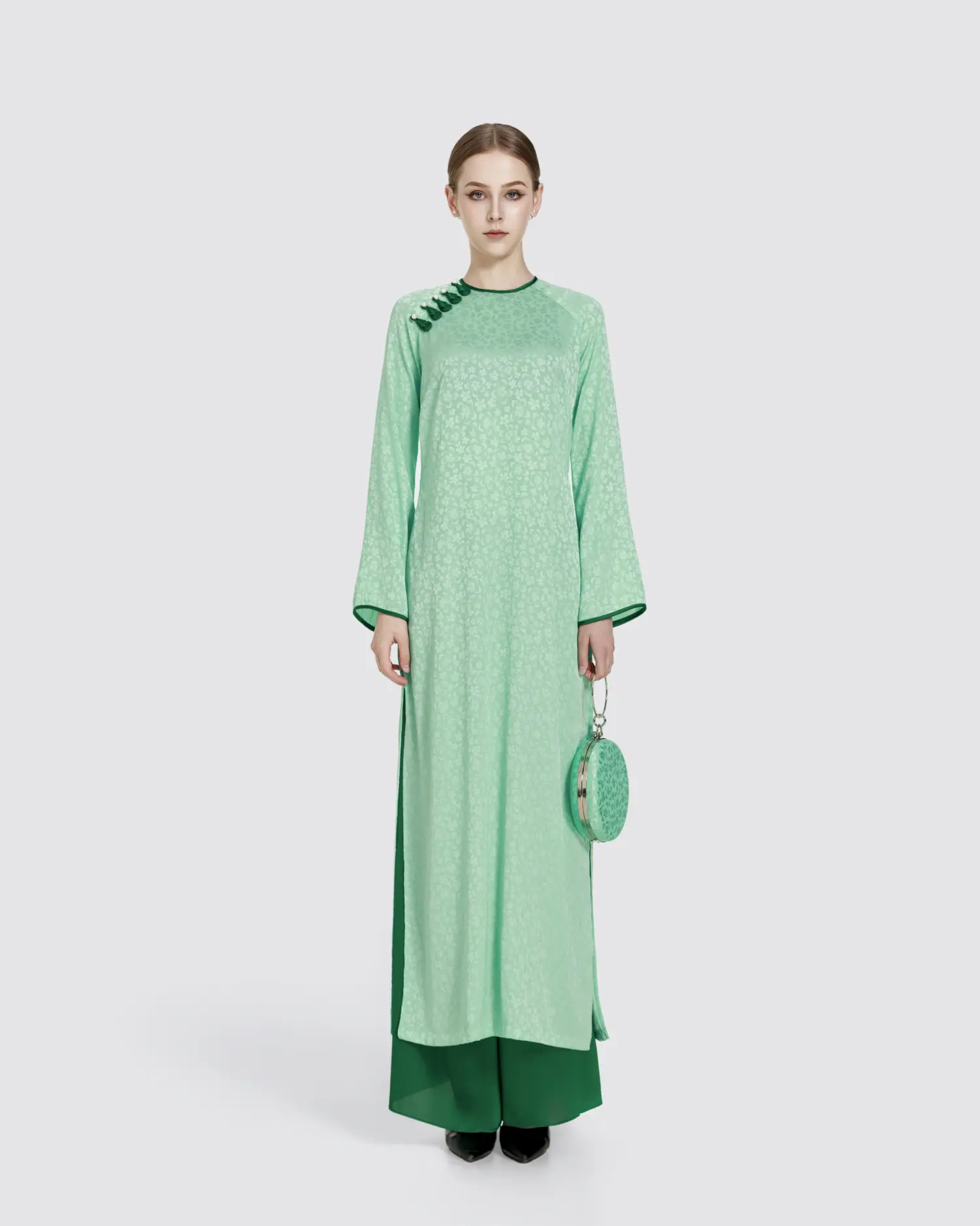 Woman in elegant green long dress with round purse, standing against a plain background.