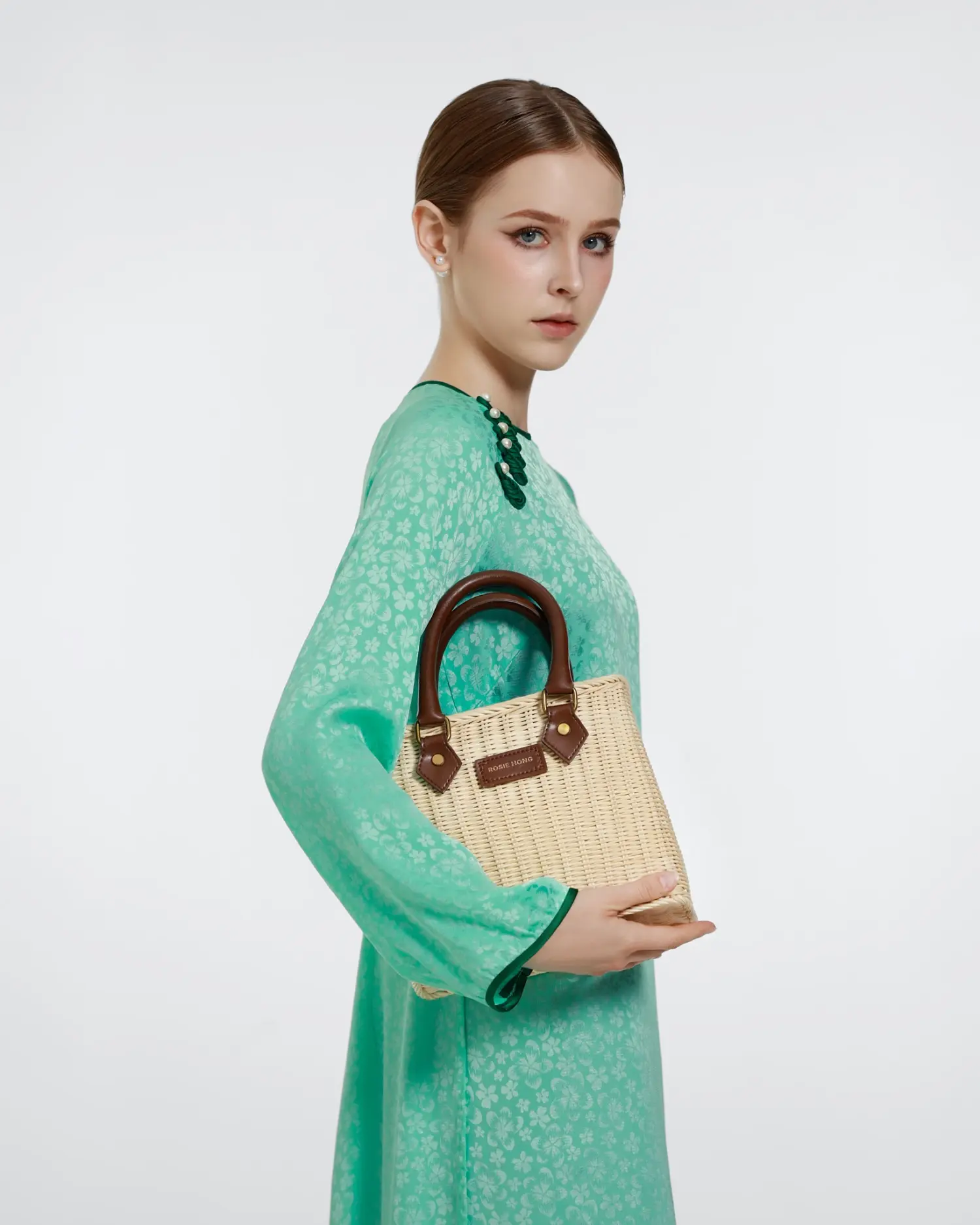 Woman in a green dress holding a stylish woven handbag with leather handles.