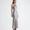 Woman in elegant silver halter dress with heels, side profile against plain white background.
