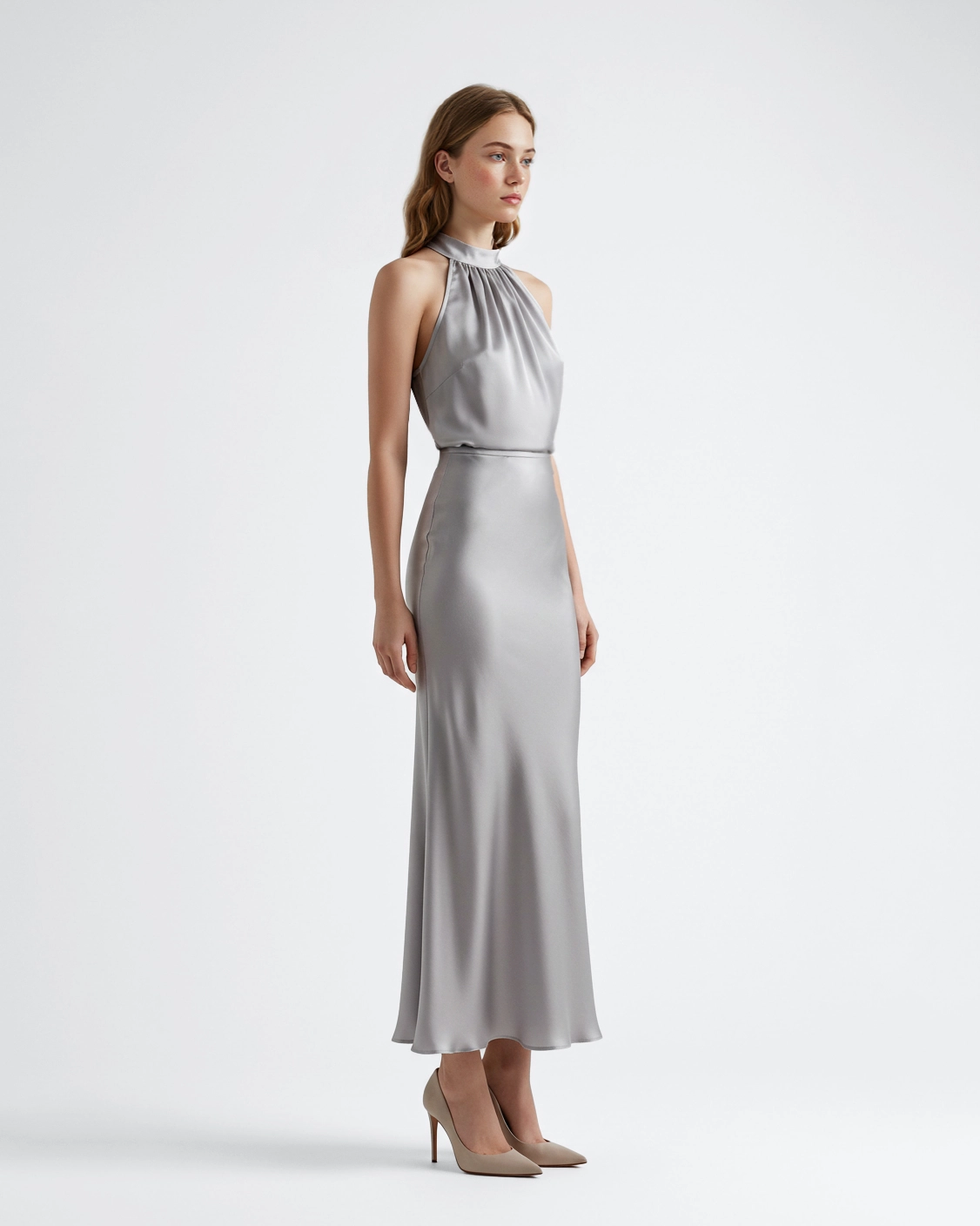 Woman in elegant silver halter dress with heels, side profile against plain white background.