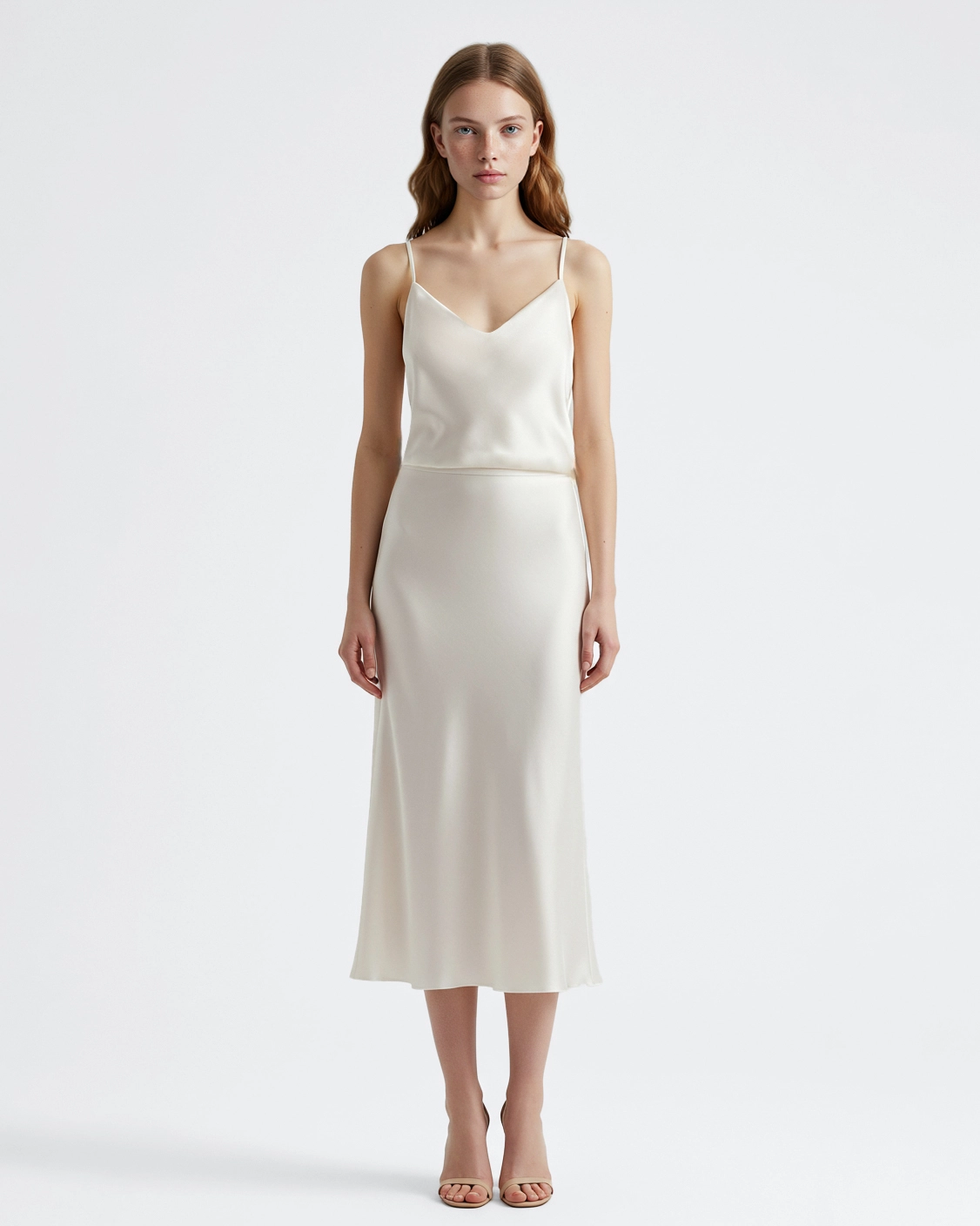 Woman in elegant ivory satin slip dress with thin straps, standing against a plain background.