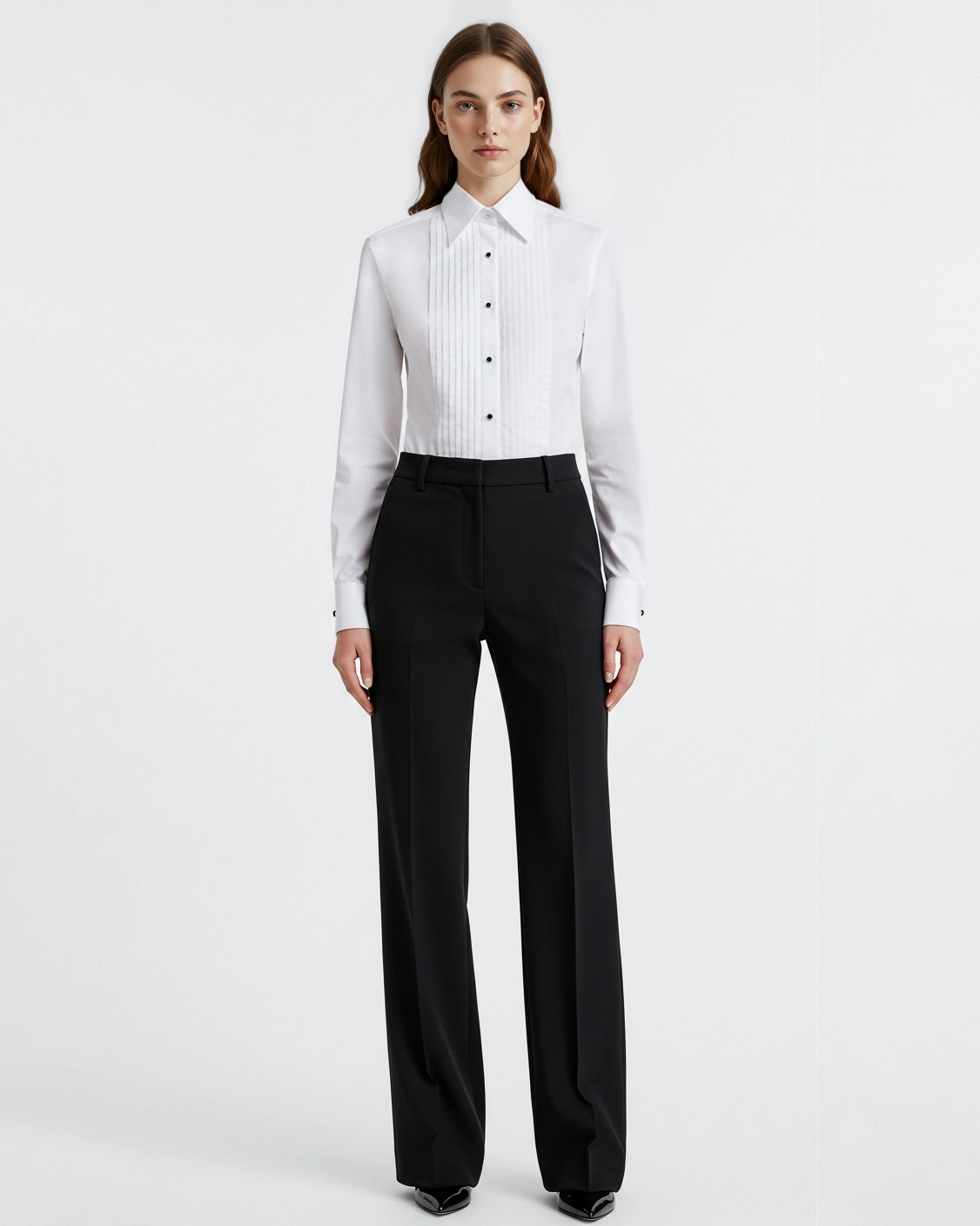 Woman wearing a white blouse and black trousers in a minimalist studio setting.