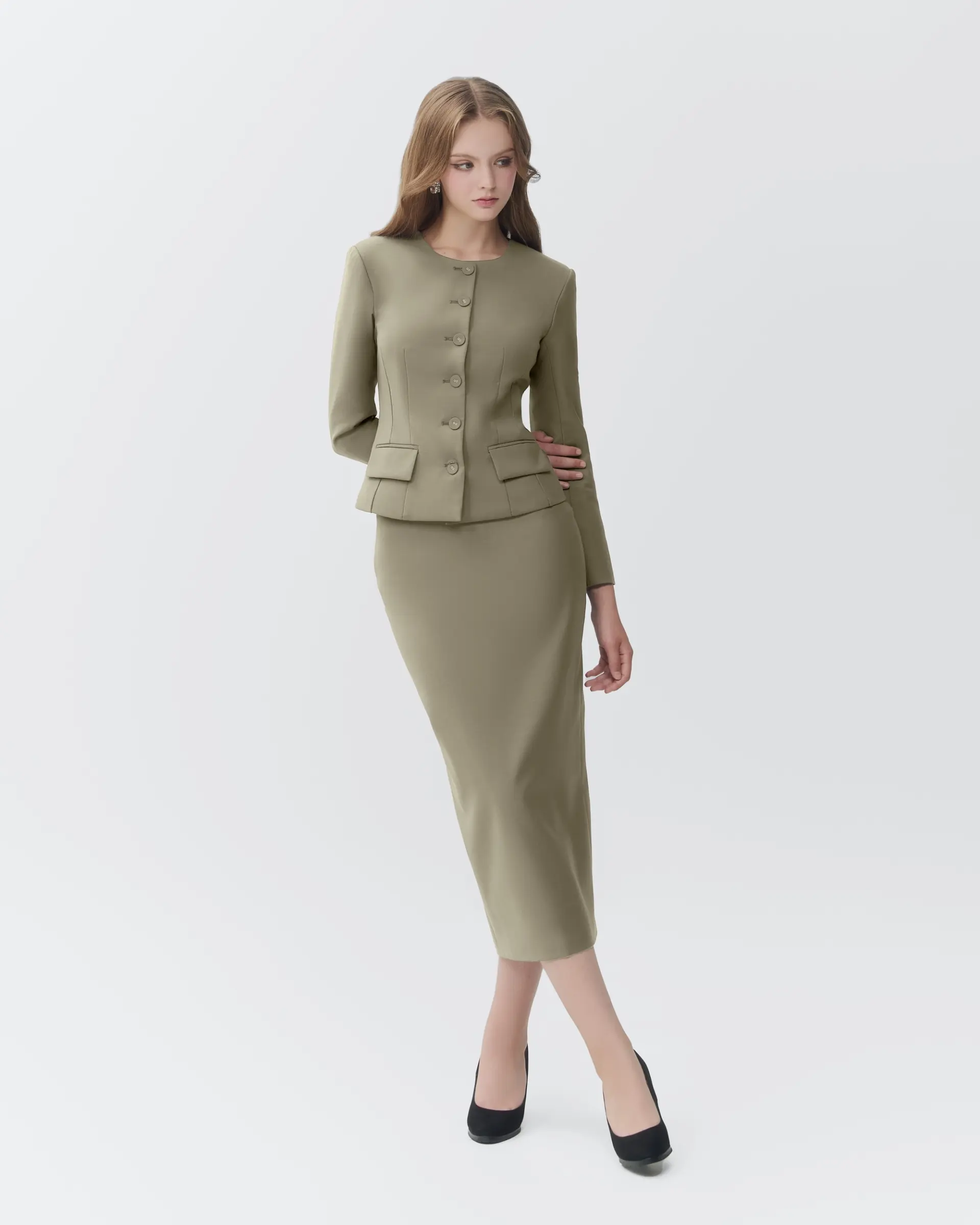 Woman in olive skirt suit with long sleeves and button detail, standing gracefully in black heels.