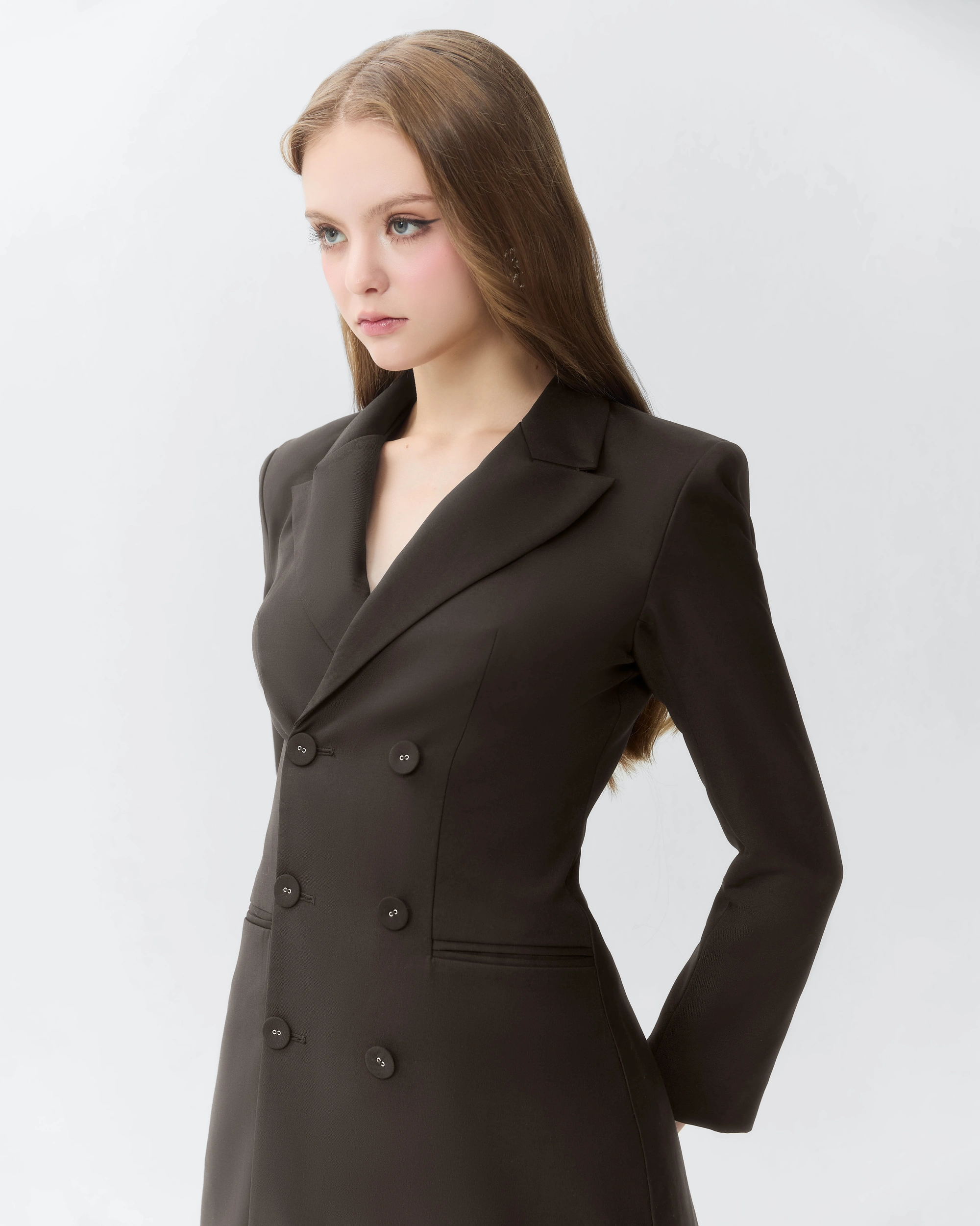 Woman in a stylish black blazer with a button detail, standing confidently against a neutral background. Fashion portrait.