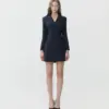 Woman in a stylish black blazer dress and heels, posing confidently against a plain background.