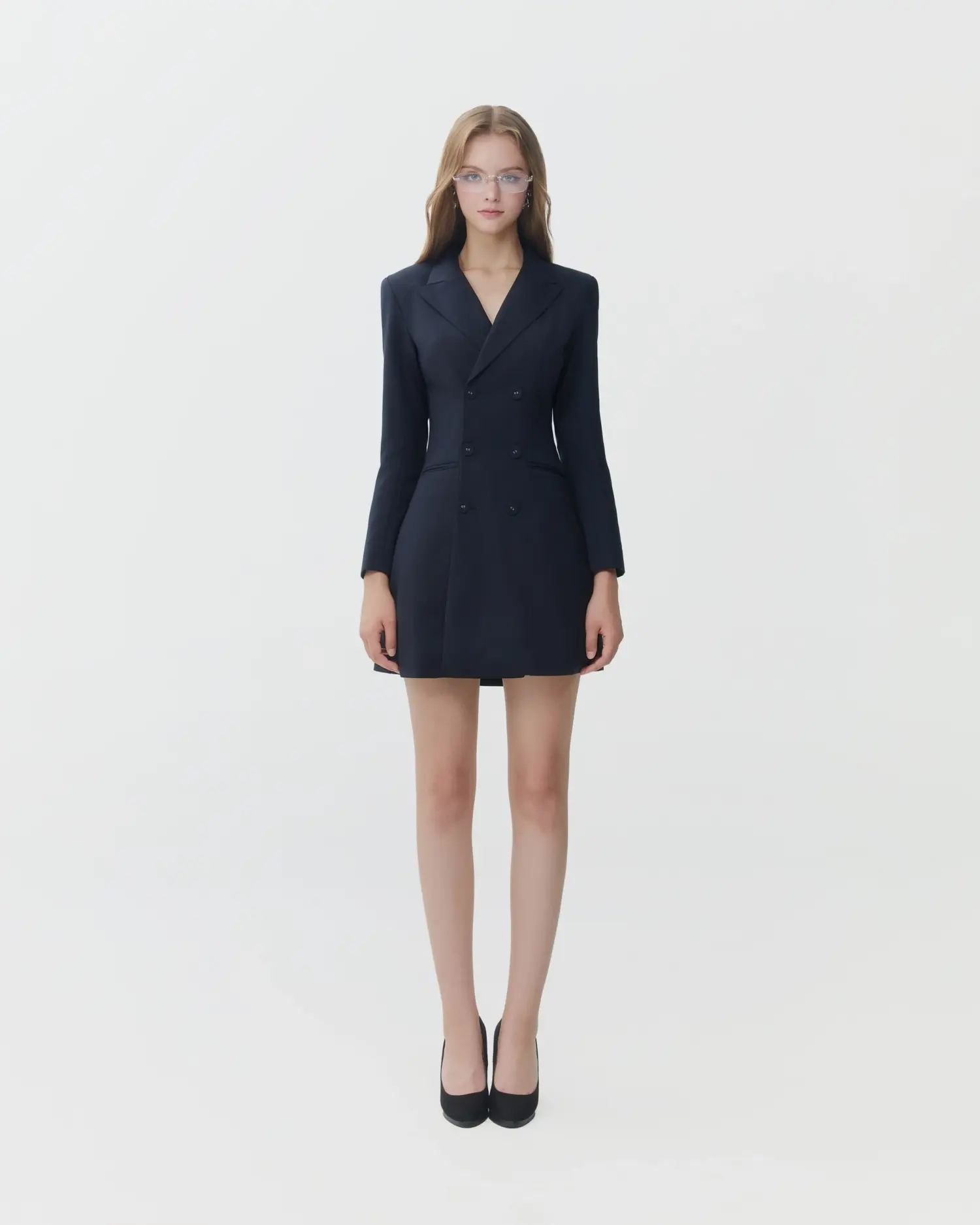 Woman in a stylish black blazer dress and heels, posing confidently against a plain background.