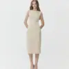 Woman in elegant beige dress with hands in pockets, standing on a white background.