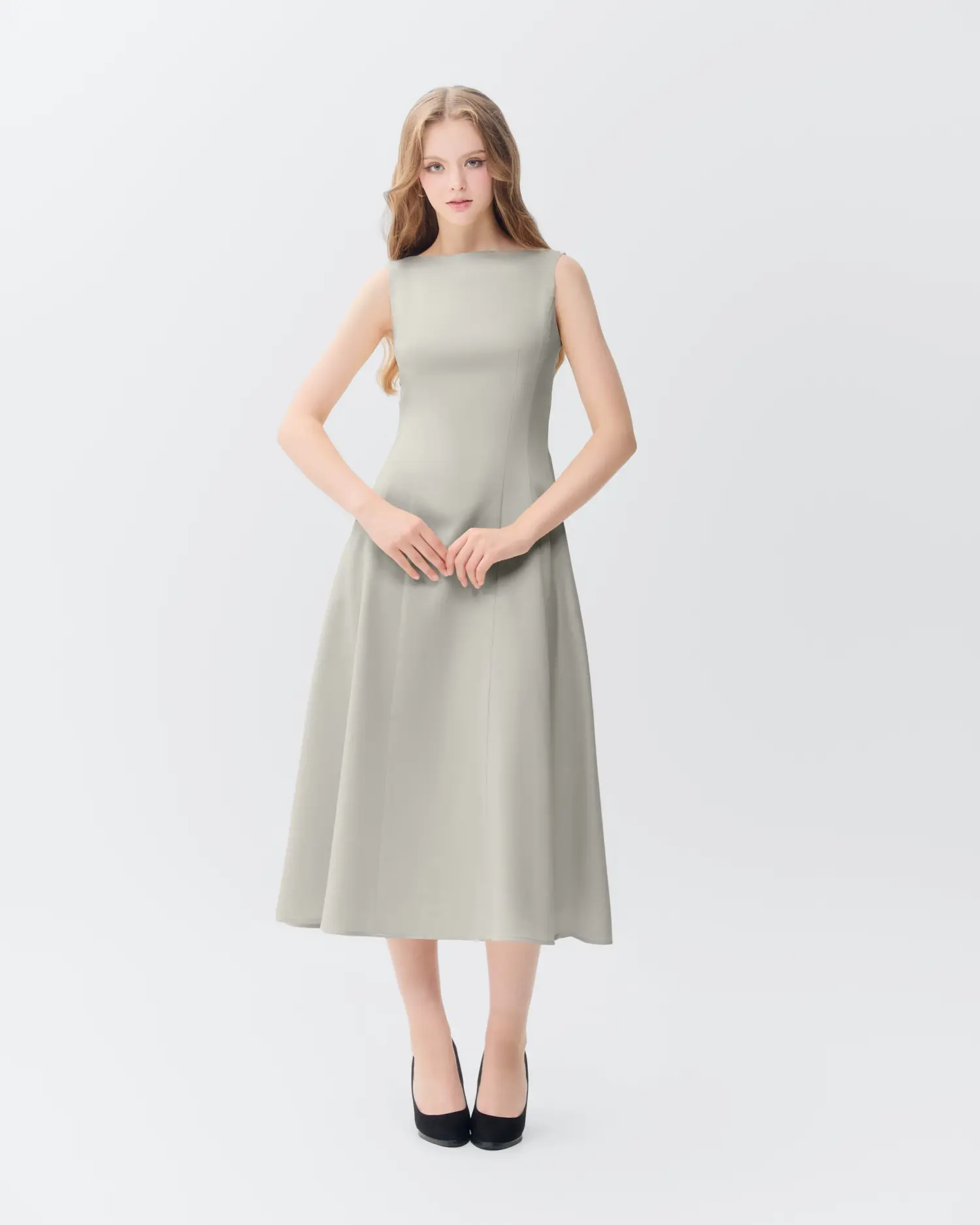 Elegant woman in a sleek gray dress with black heels, standing against a minimalist white background.