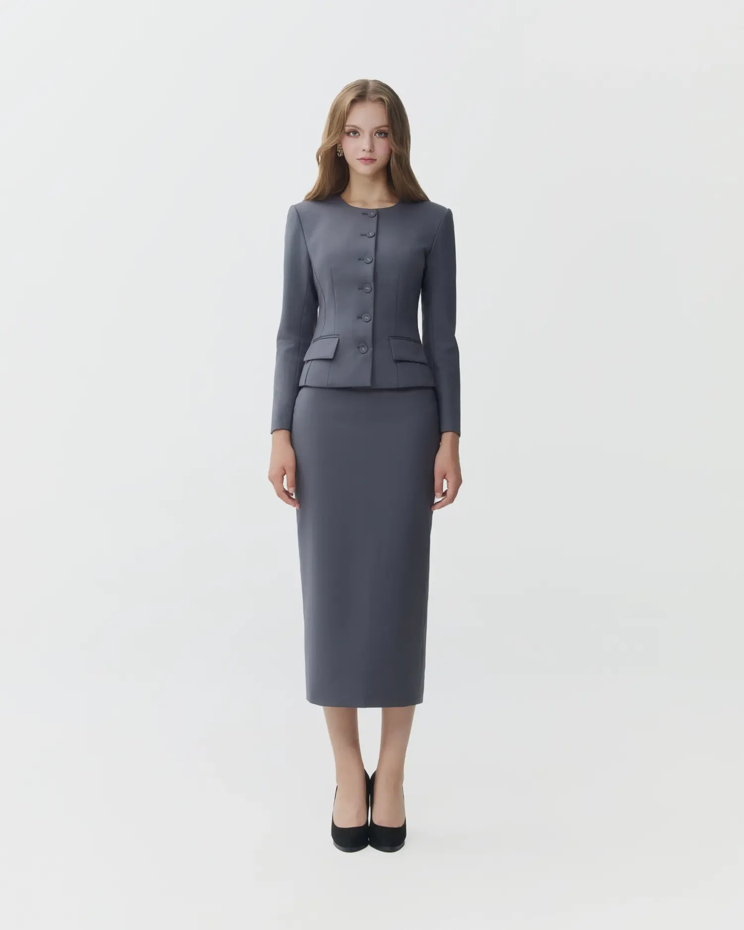 Woman in formal gray suit with long skirt and black heels, standing against a white background.
