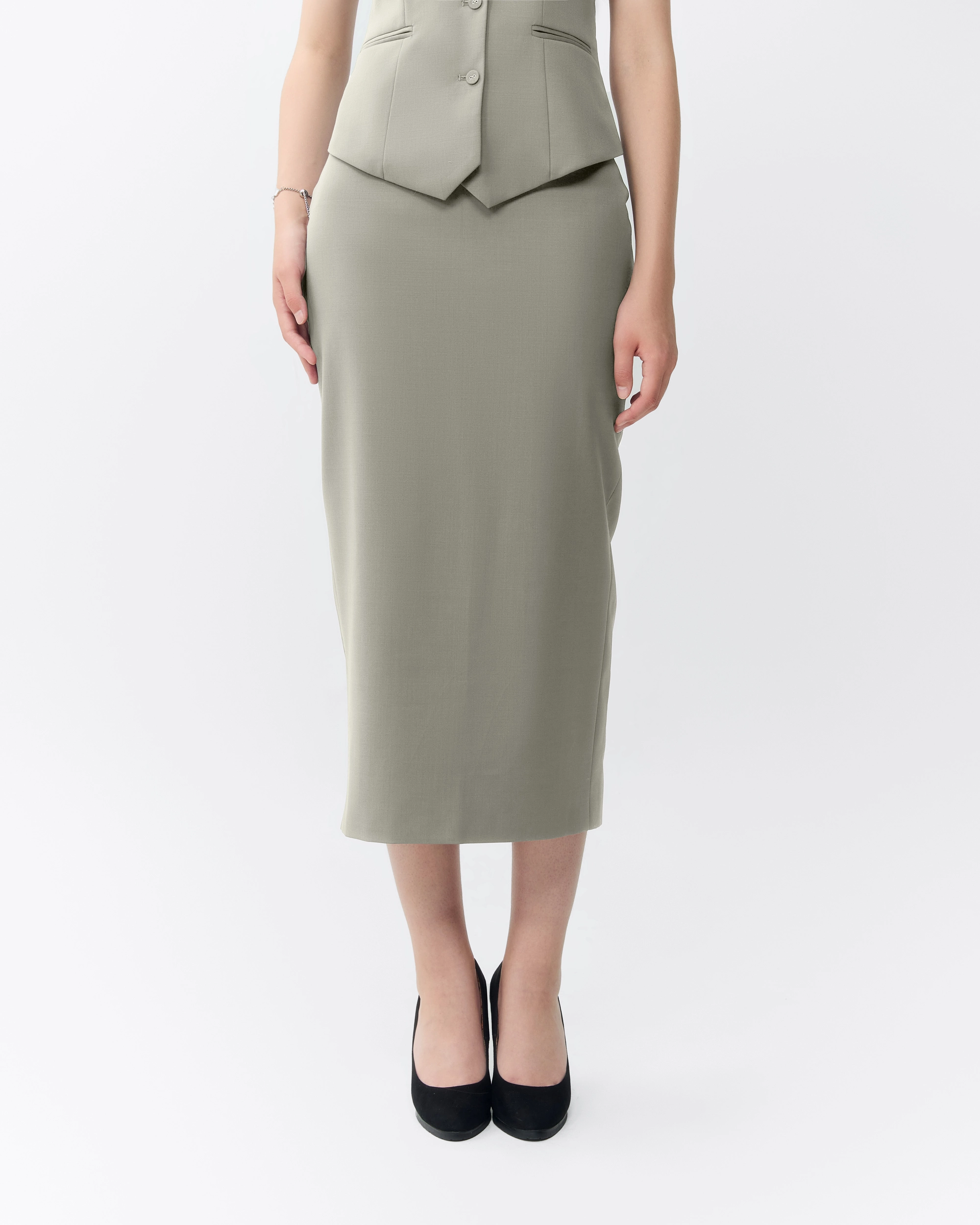 Woman in a tailored gray skirt suit with black heels, standing against a white background.