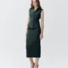 Woman in stylish dark green vest and skirt outfit against a plain background, showcasing modern fashion elegance.