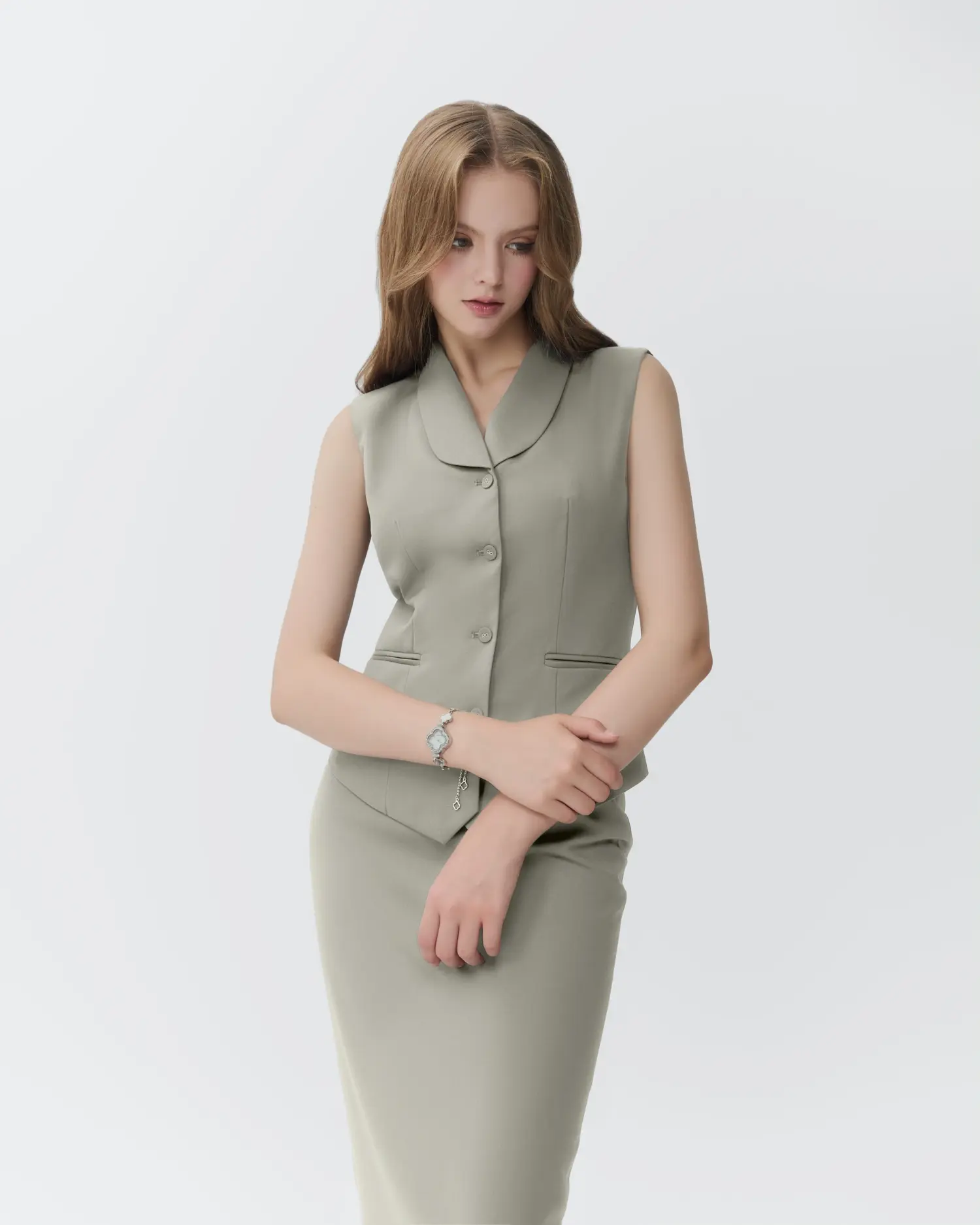 Woman in a tailored grey suit poses on a white background, showcasing formal fashion with a bracelet accessory.