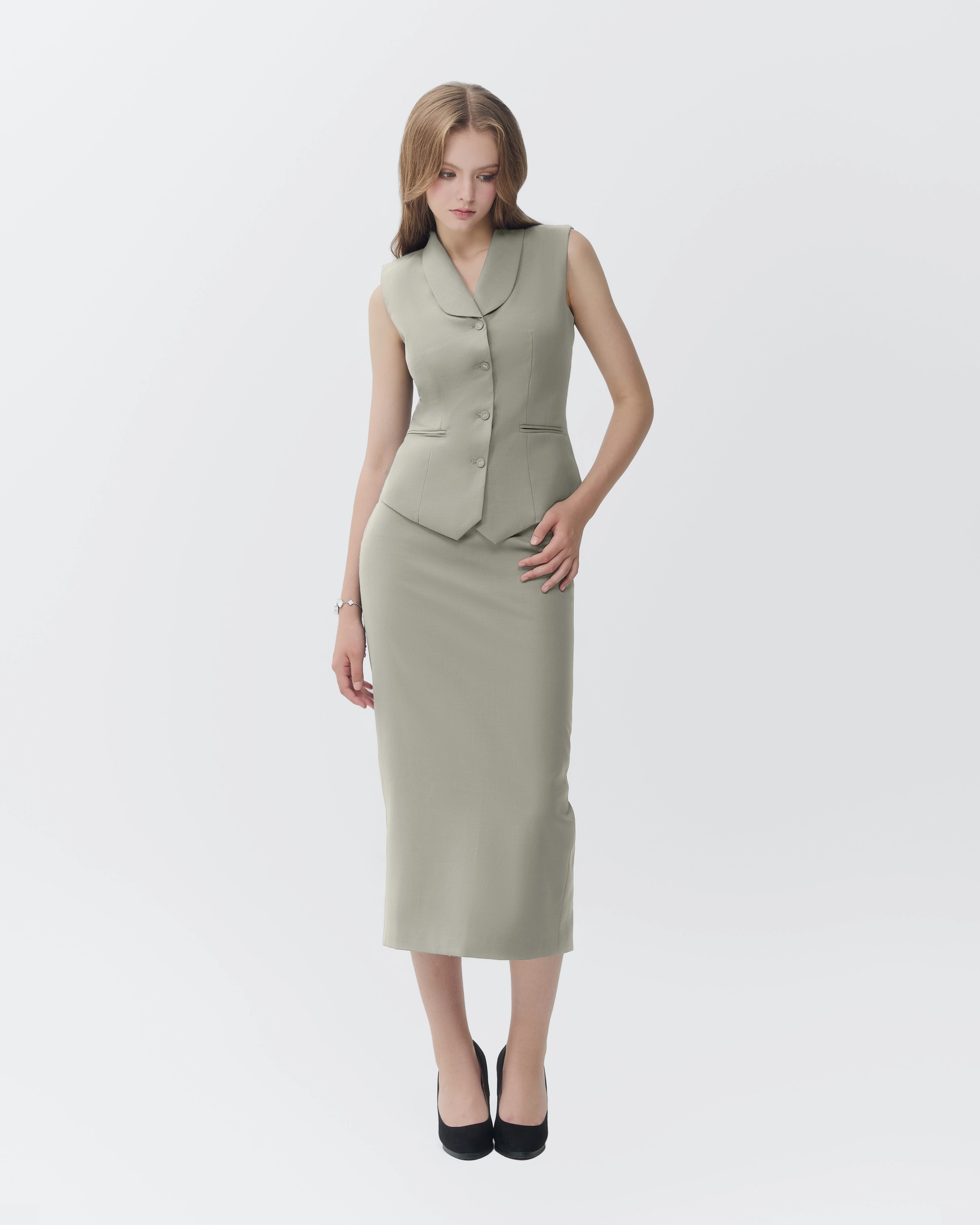Woman in a stylish grey vest and skirt set on a white background, showcasing modern fashion attire.