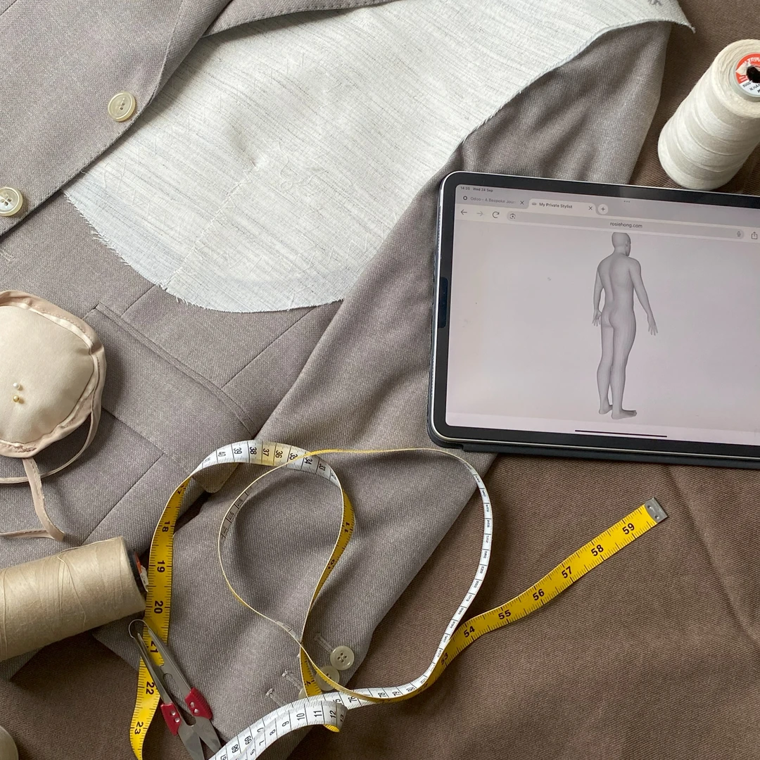 Tailoring essentials: suit fabric, tablet, measuring tape, needles, and thread on a workbench.