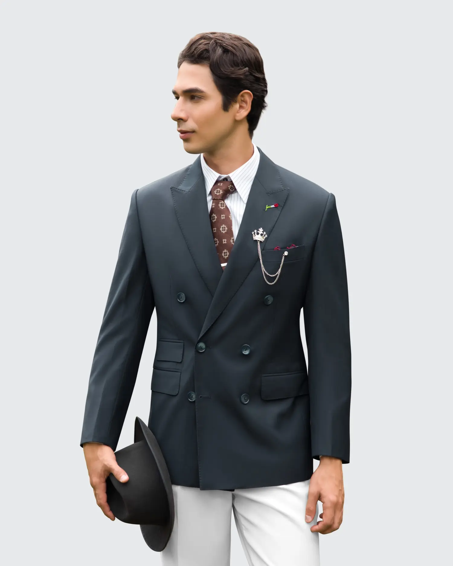 Man in tailored suit with accessories and holding a hat, looking left, stylish and elegant formal attire.