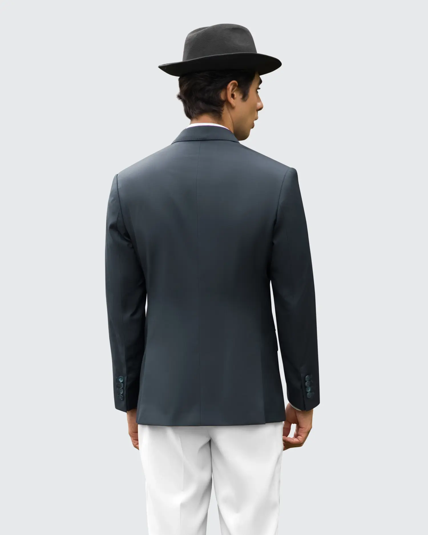 Man in black hat and jacket with white pants, seen from behind against a plain background.