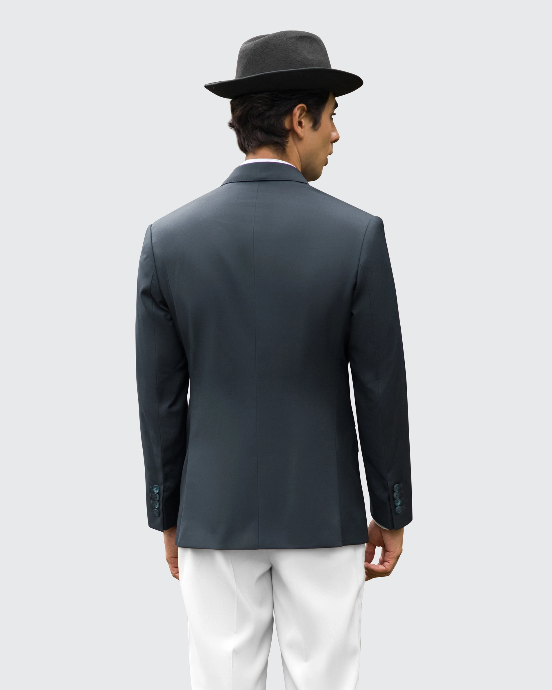 Man in black hat and jacket with white pants, seen from behind against a plain background.