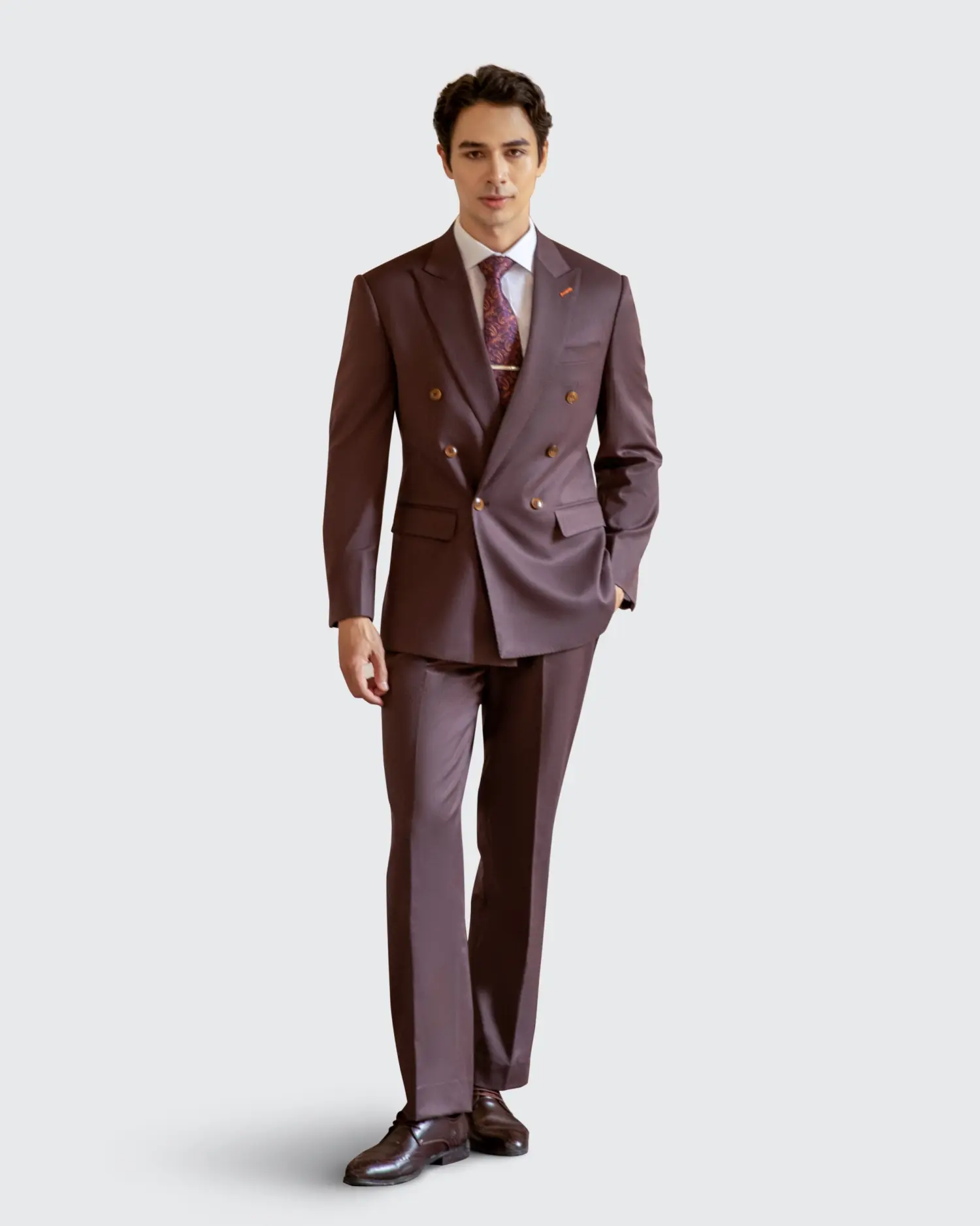 Man in a stylish brown double-breasted suit, white shirt, and patterned tie on a light background.