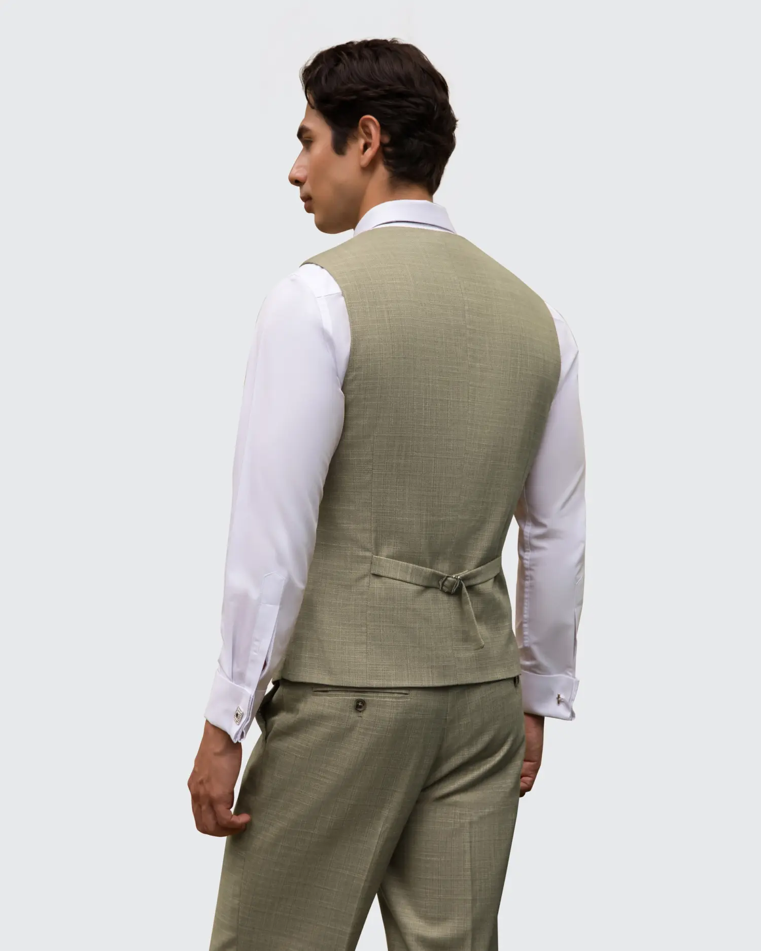 Man wearing a light green suit vest over a white shirt, viewed from the back against a plain background.