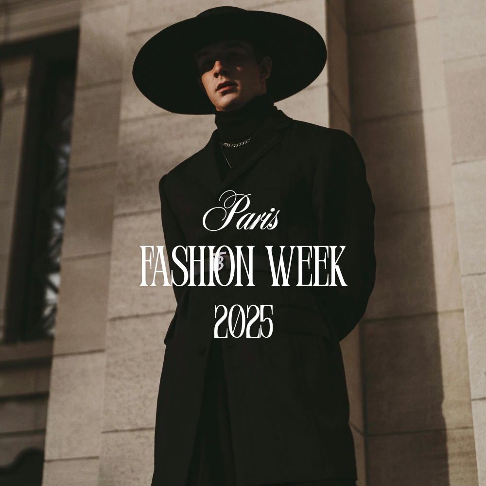 Model in black outfit and wide-brim hat at Paris Fashion Week 2025, standing against a stone building.