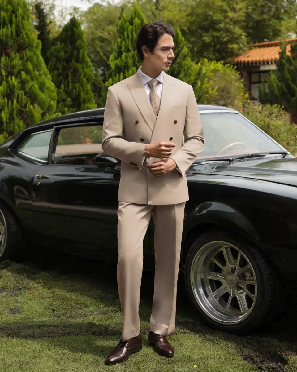 Man in beige suit standing by black vintage car outdoors.