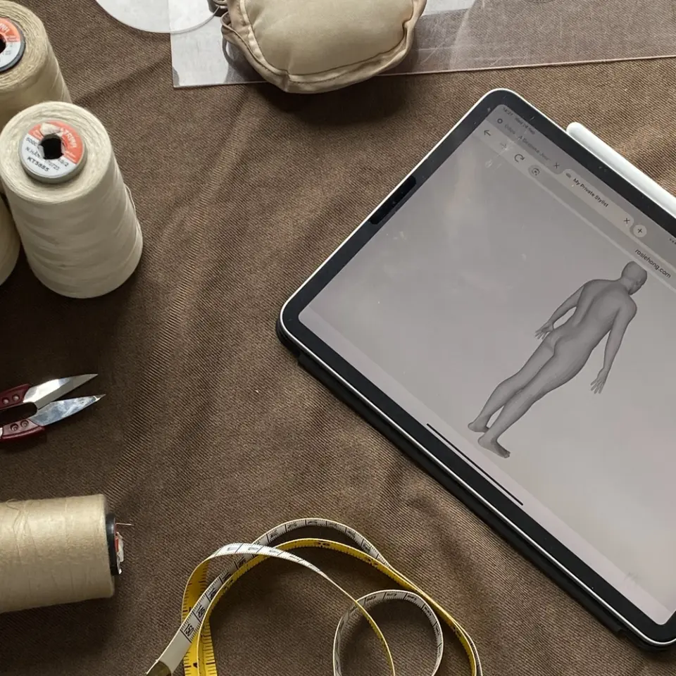 Tablet with 3D model, spools of thread, and measuring tape on brown fabric, showcasing sewing preparation.