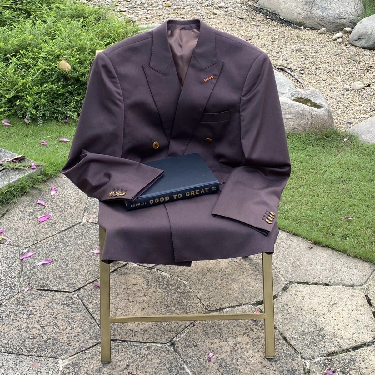 Brown tailored blazer on chair with Good to Great book, outdoor setting with grass and stone path.