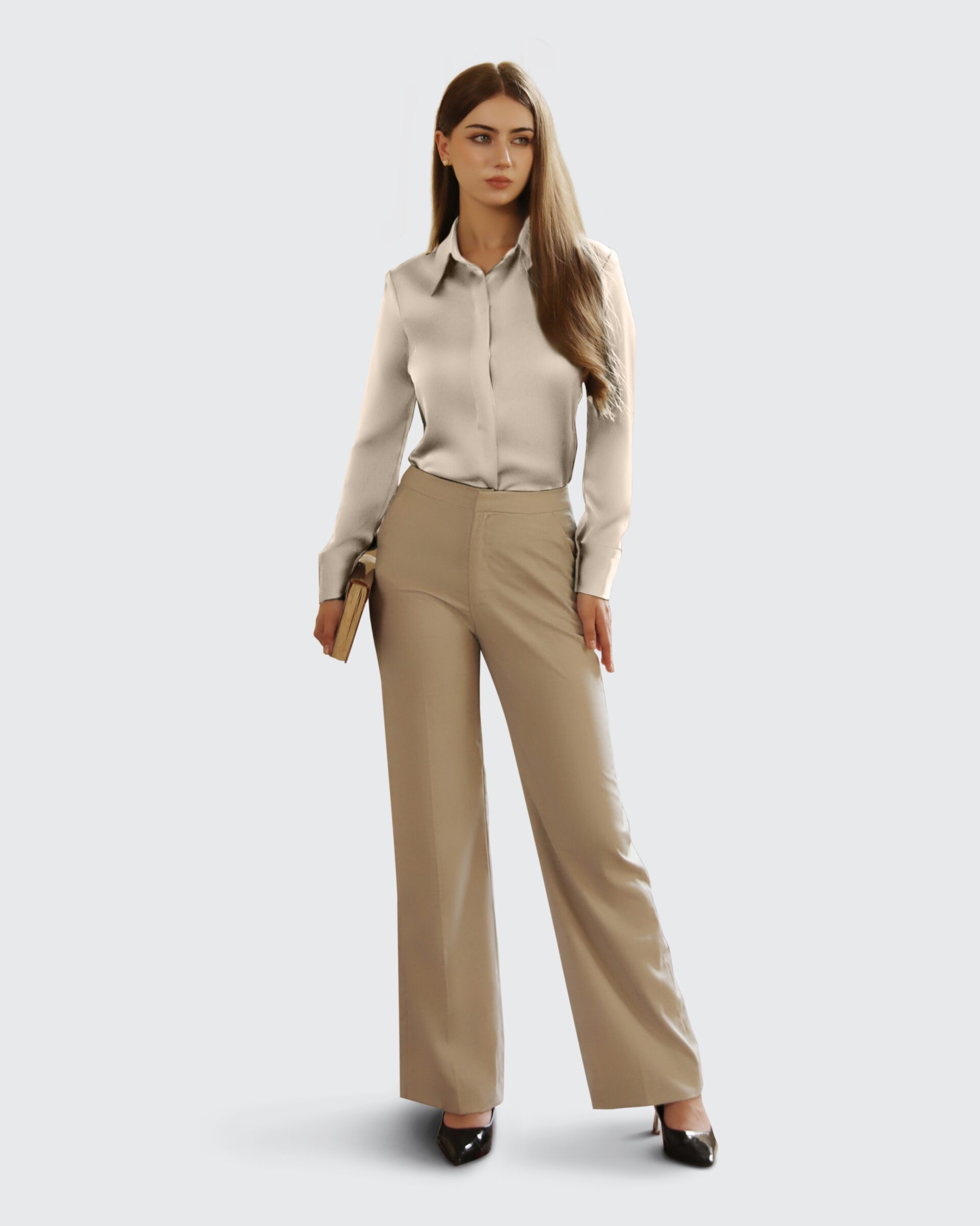 Businesswoman in a beige outfit holding a book stands confidently against a gray background.