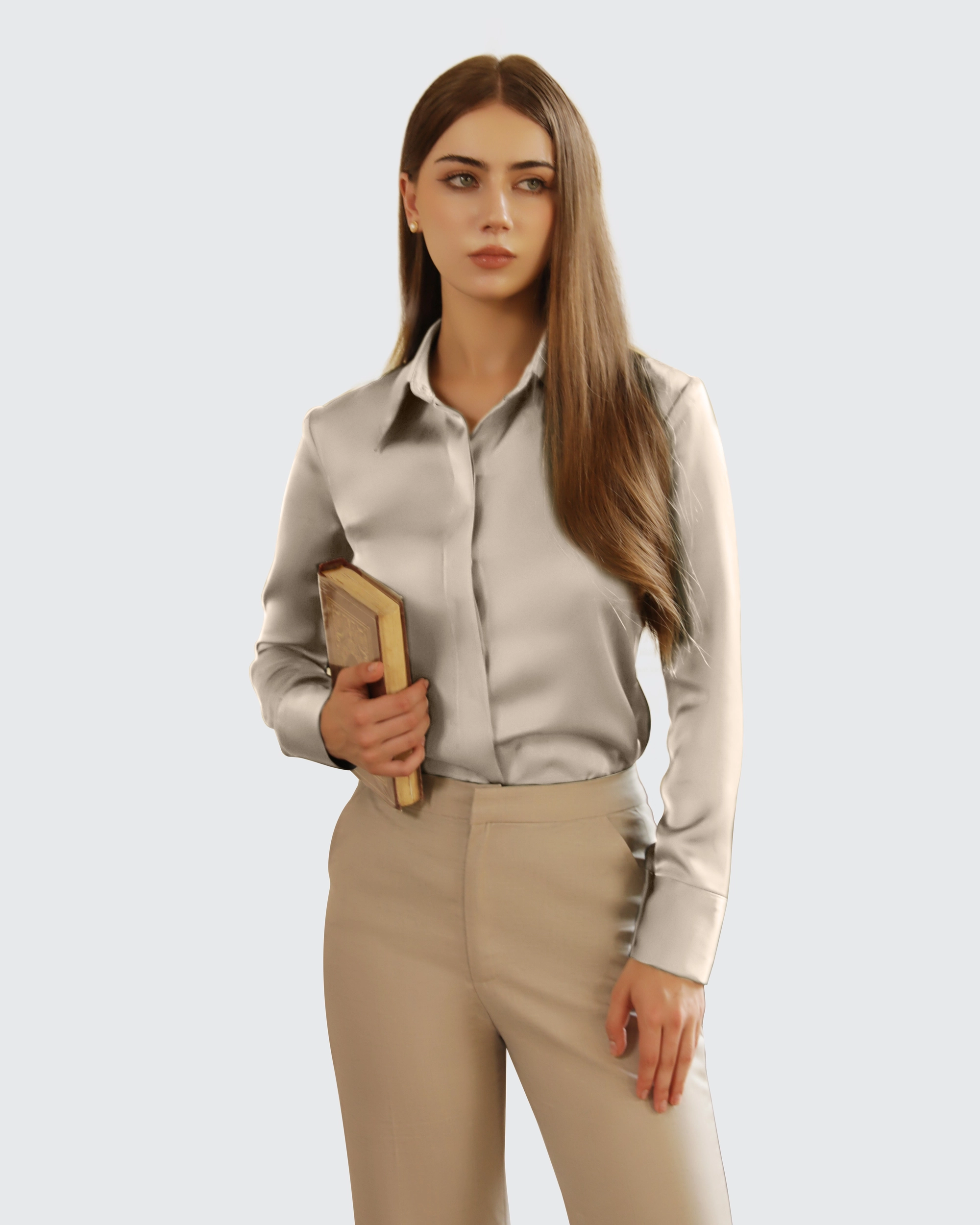 Young woman in beige outfit holding a book, standing against a neutral background. Elegant fashion style.