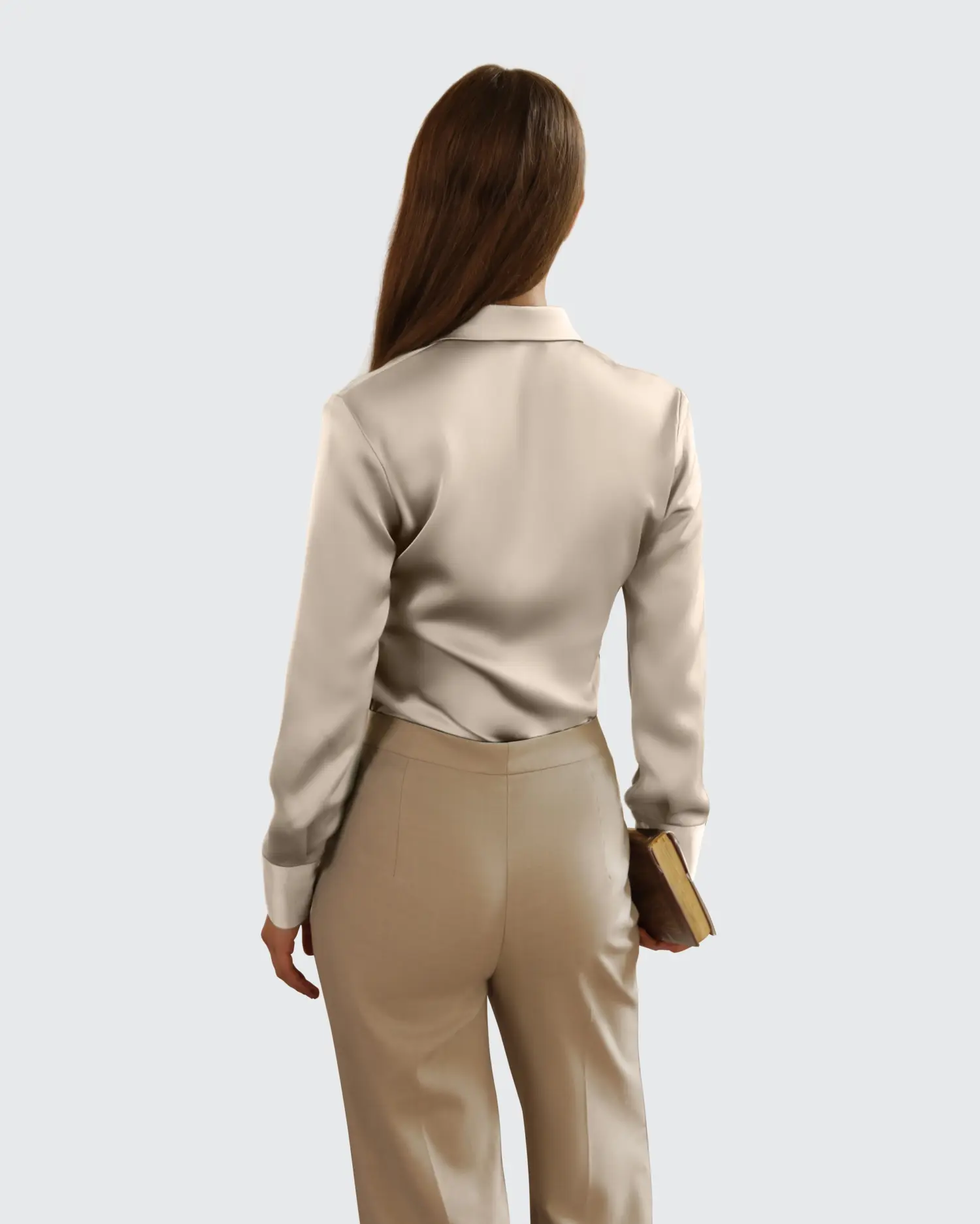 Woman in business attire holding a book, beige suit and long hair, viewed from the back against a plain background.