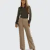 Woman in professional attire holding a book; wearing green blouse and beige trousers. Business fashion concept.