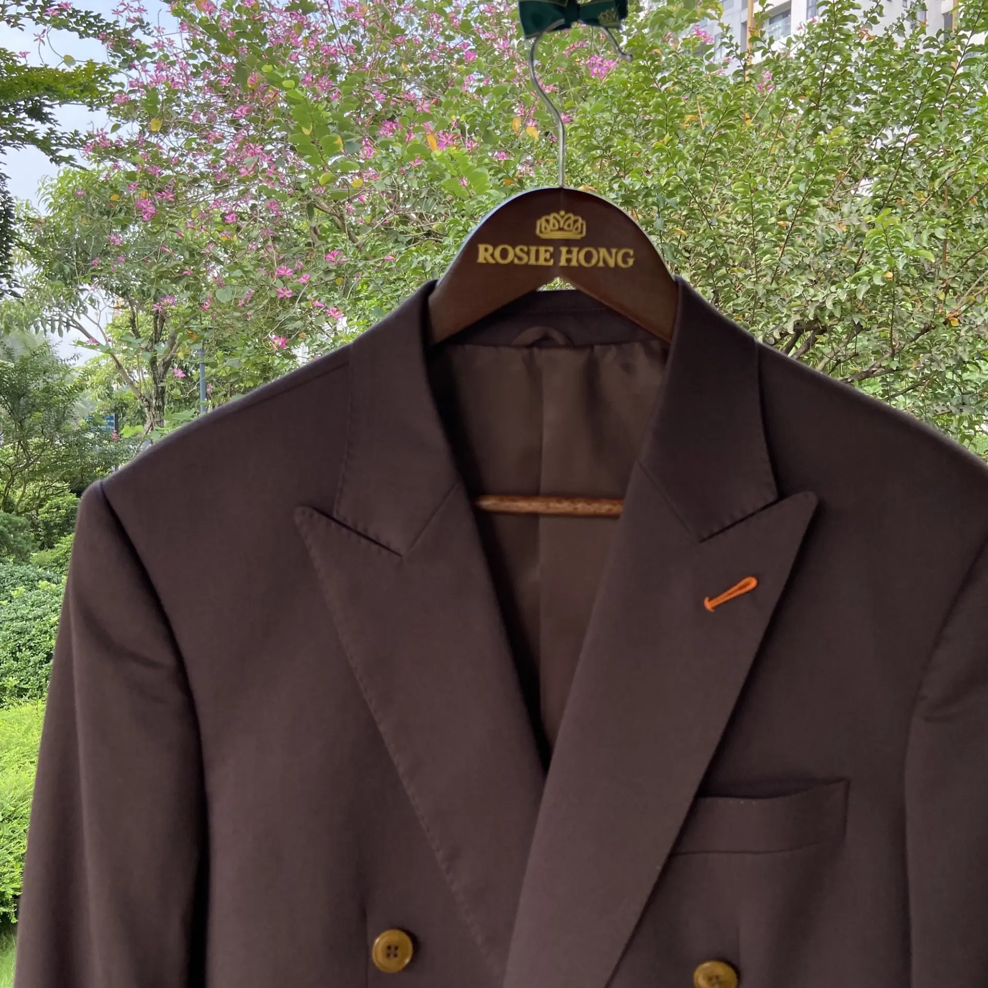 Brown suit jacket on hanger with trees in the background, labeled Rosie Hong.