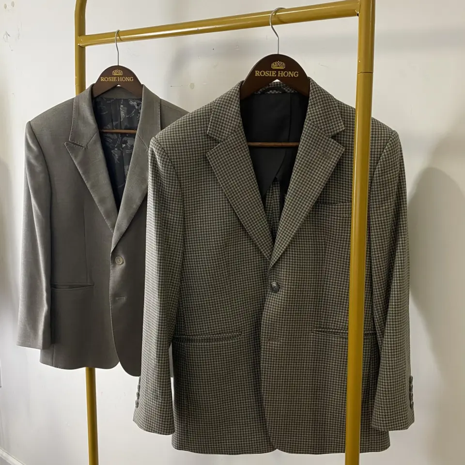 Two elegant blazers on hangers against a light background; one is grey, the other is a checkered pattern.