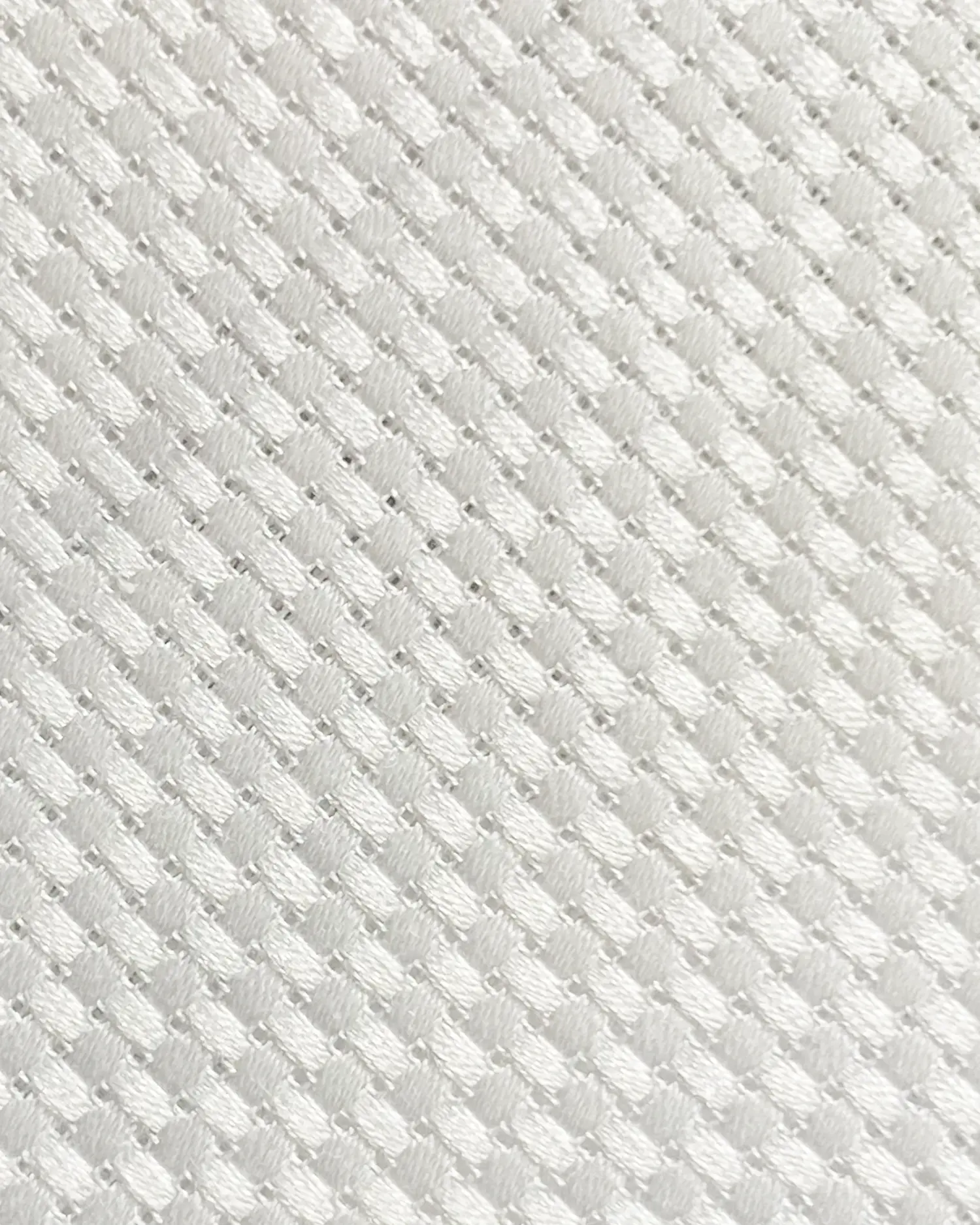 Close-up of a white textured fabric with a waffle pattern, showing detailed weaving in a diagonal grid design.