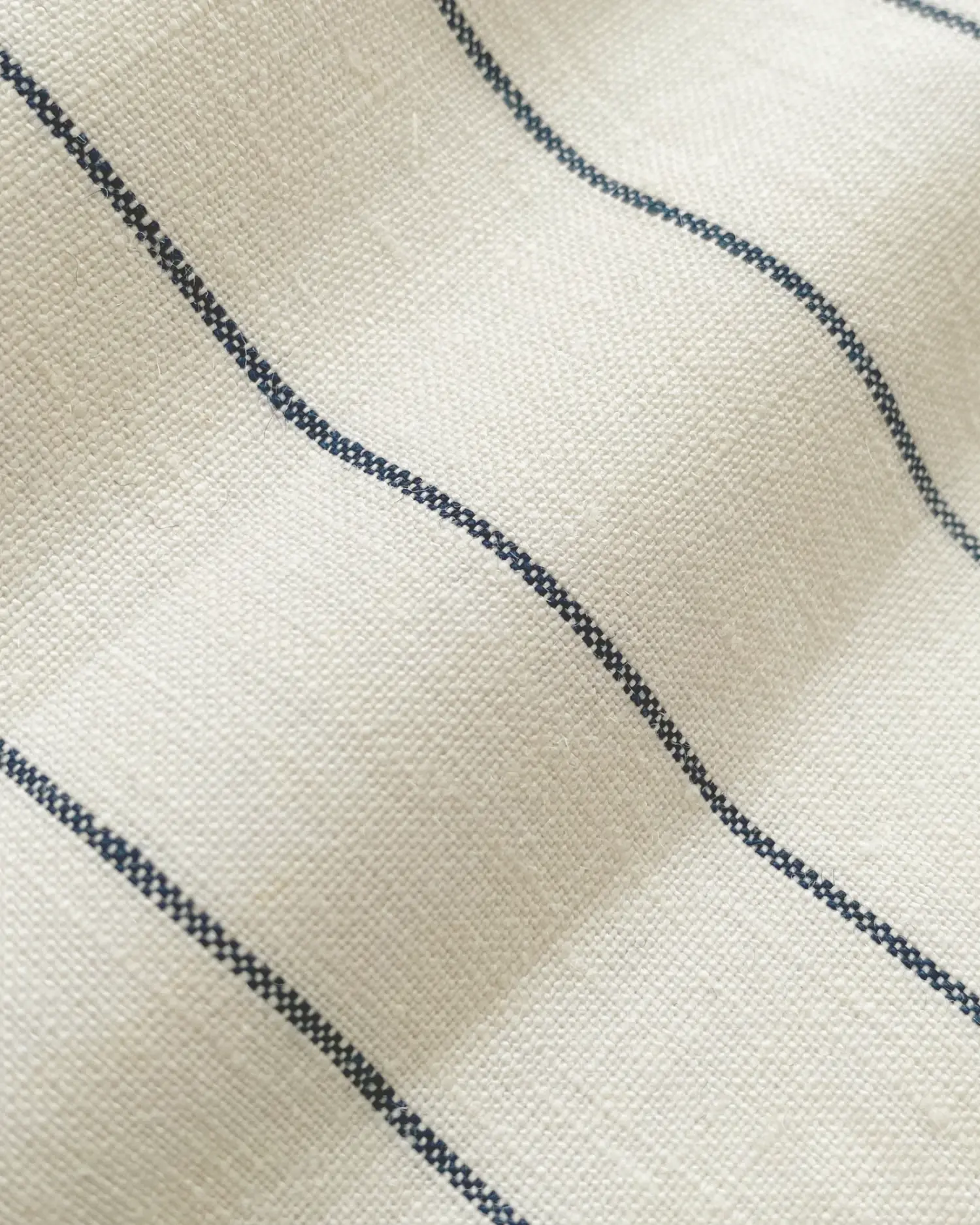 Close-up of beige fabric with blue stripes creating a minimalist pattern, enhancing texture and design elegance.