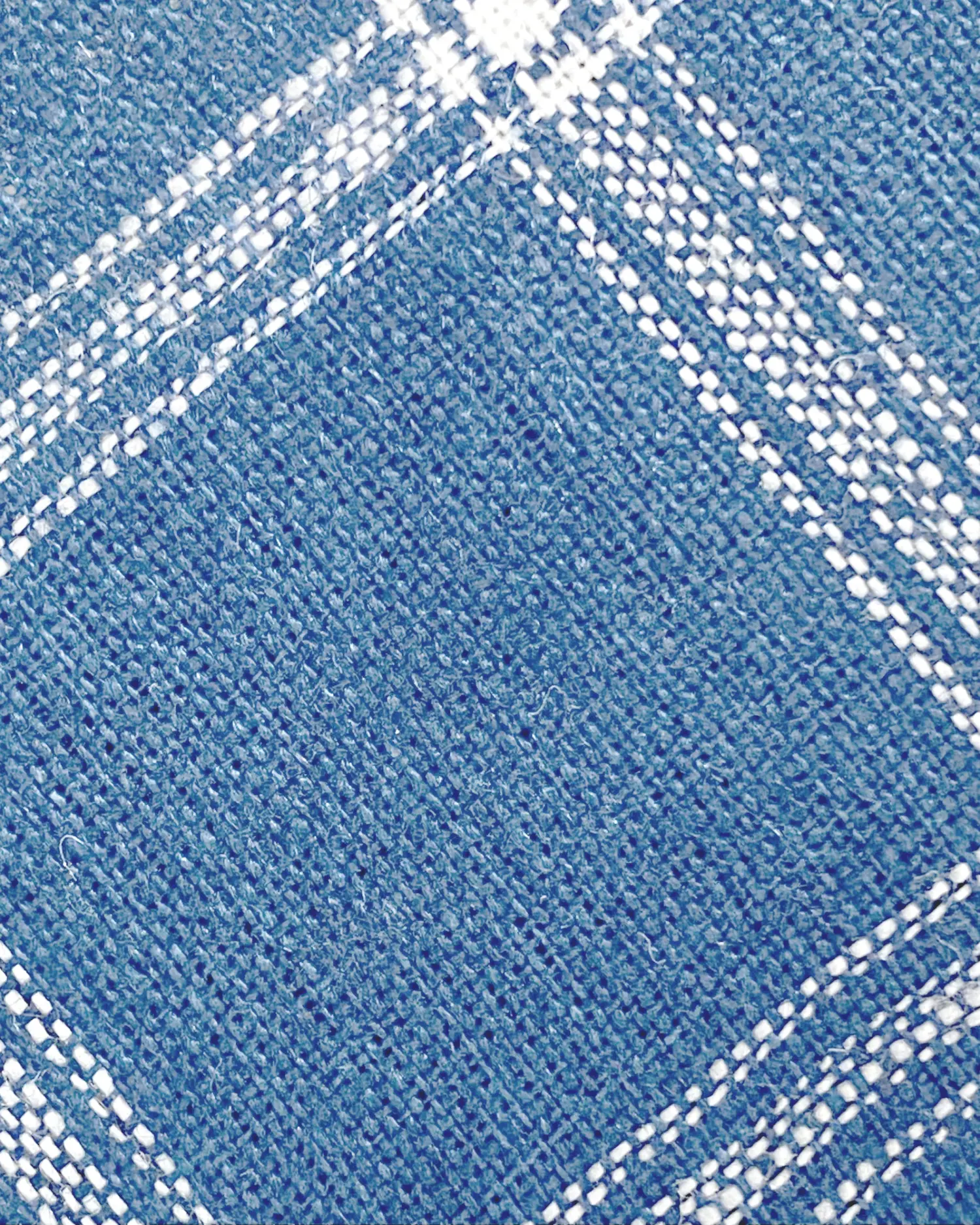 Close-up of a blue textured fabric with a white plaid pattern, showcasing intricate weaving details.
