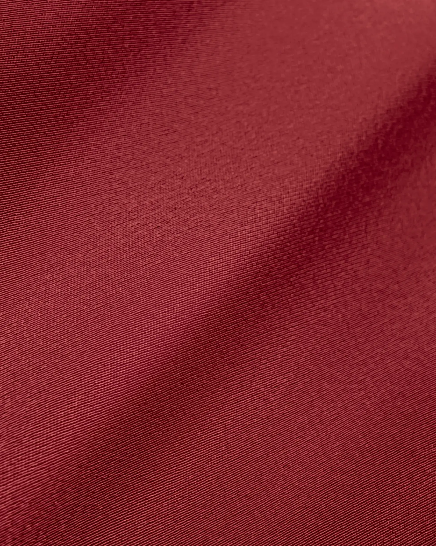 Close-up of maroon fabric texture with a smooth, shiny finish, showcasing fine textile details and rich color.